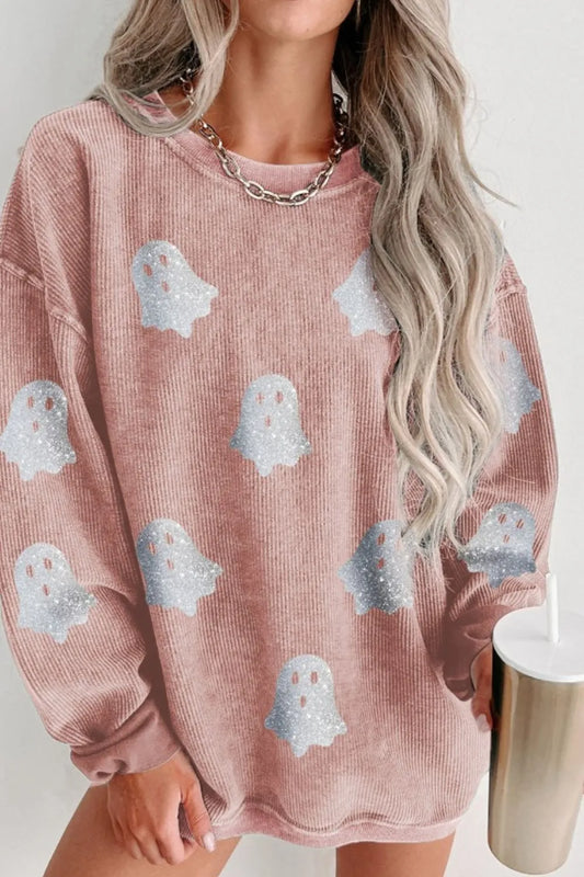 Person wearing a pink sweatshirt with ghost patterns, holding a white cup.