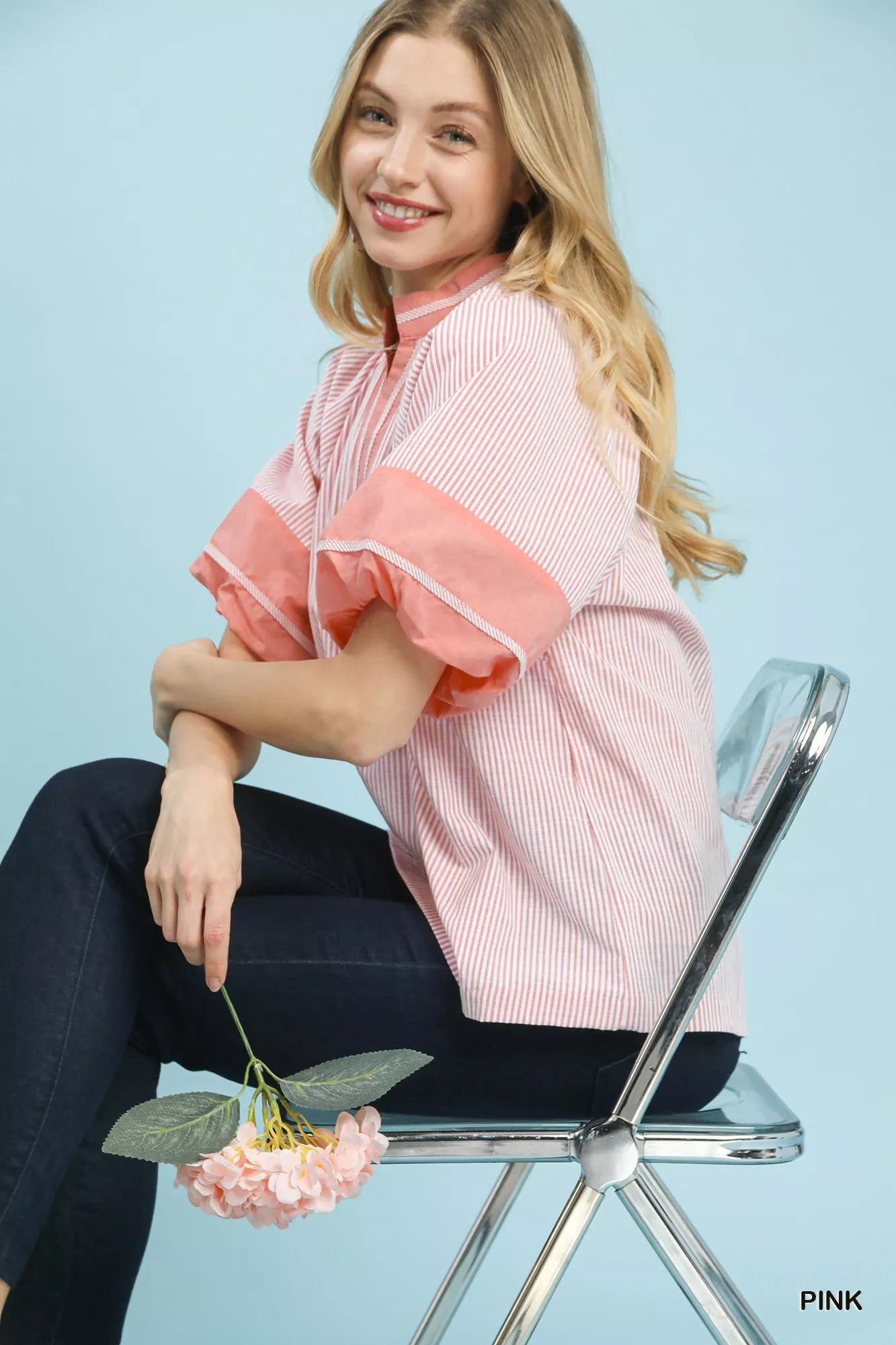 Model sitting on chair wearing Umgee pink and white striped mixed puff sleeve blouse, holding flowers