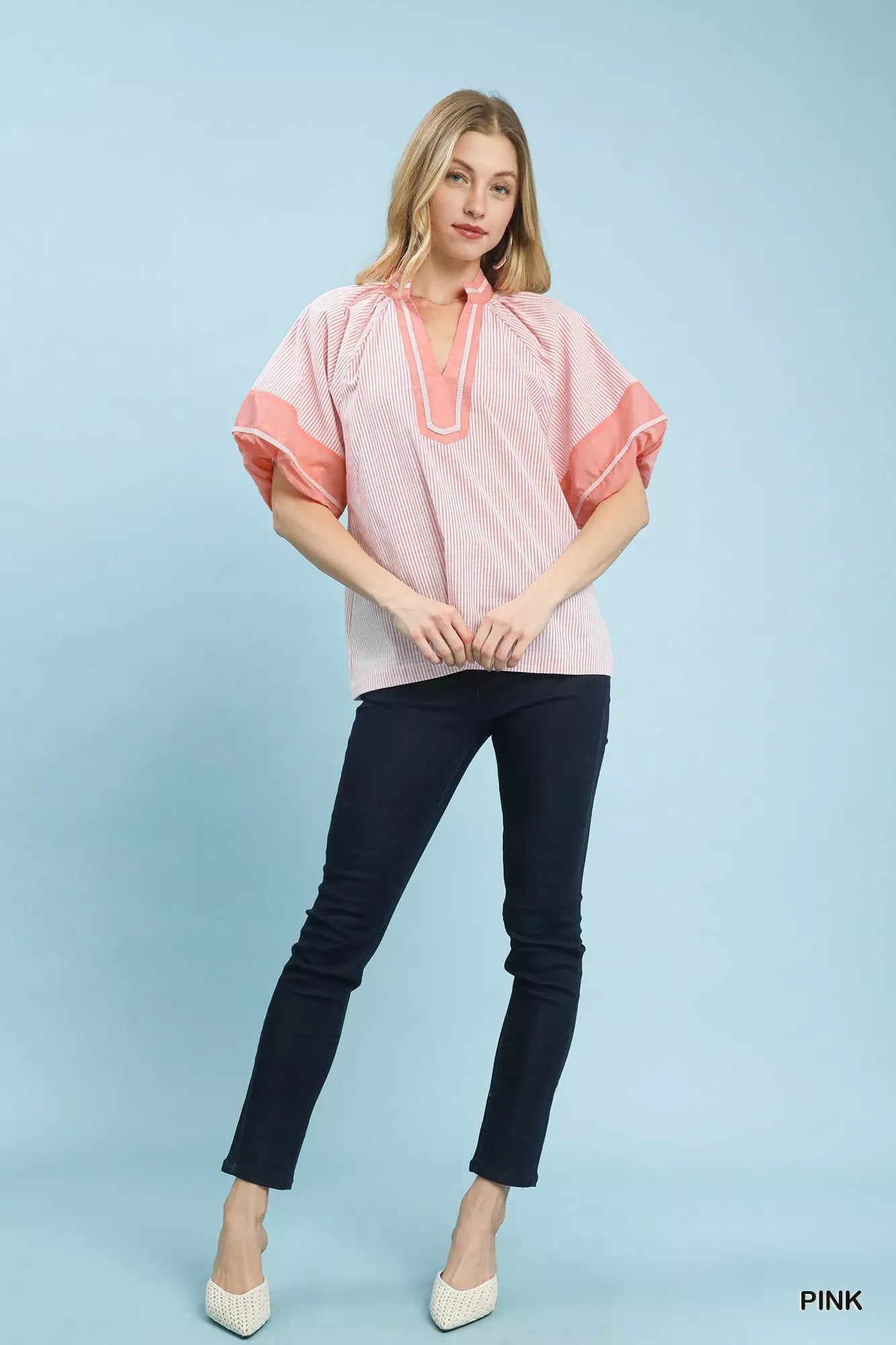 Model standing wearing Umgee pink and white striped mixed puff sleeve blouse with dark jeans and white shoes
